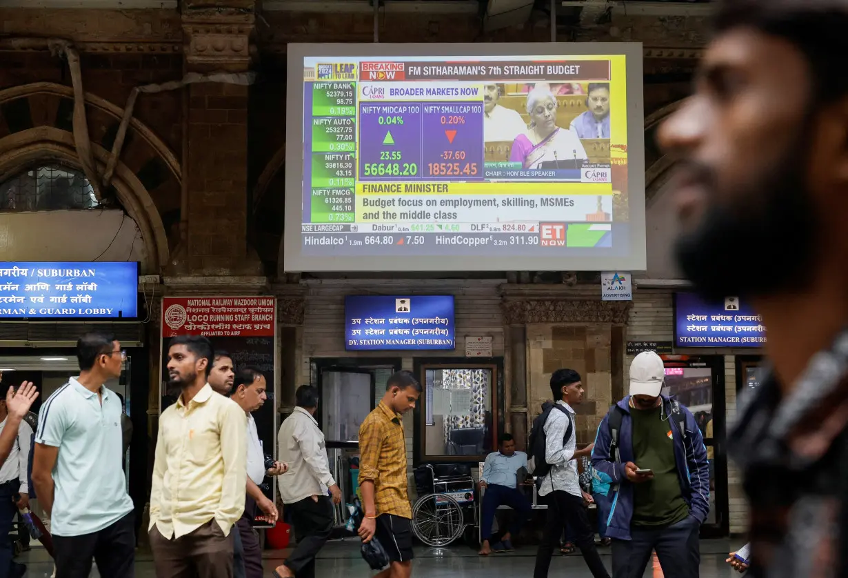 People walk past a screen displaying India's Finance Minister Nirmala Sitharaman's budget speech at a railway station in Mumbai