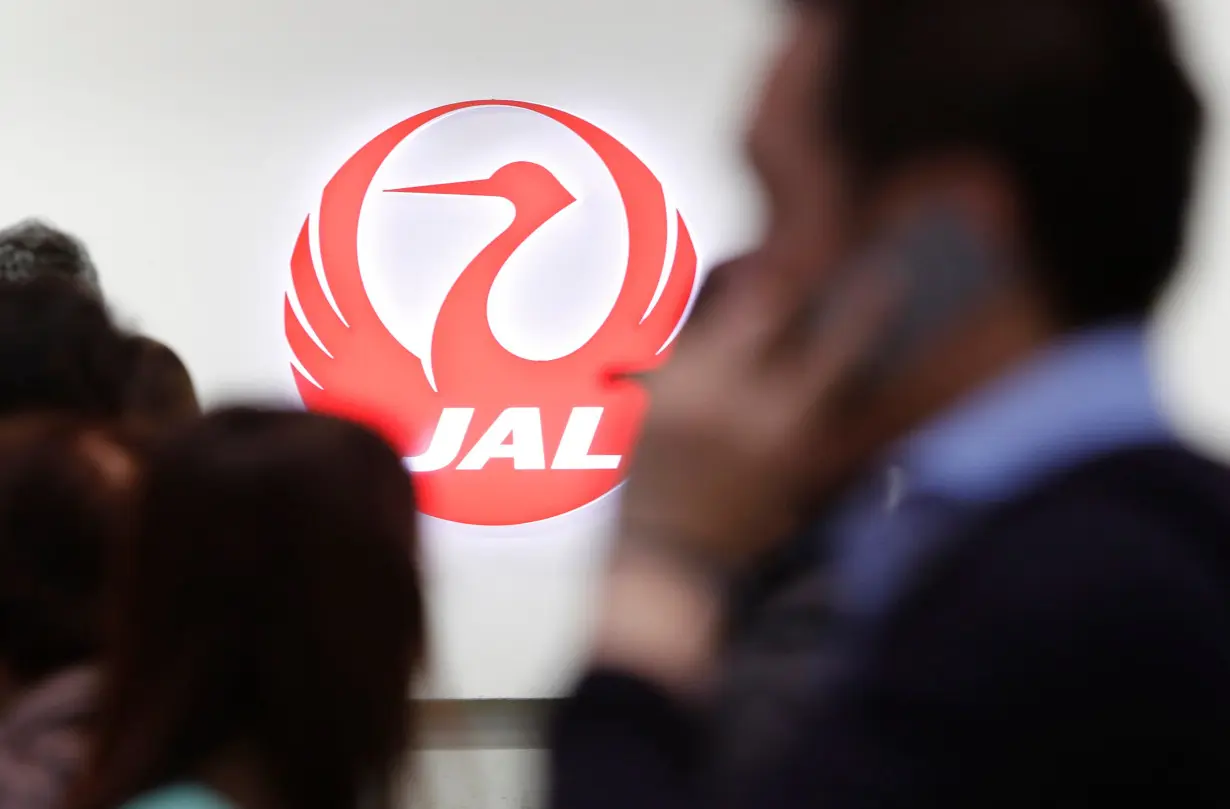 Passengers walk past the logo of Japan Airlines (JAL) at Haneda airport in Tokyo