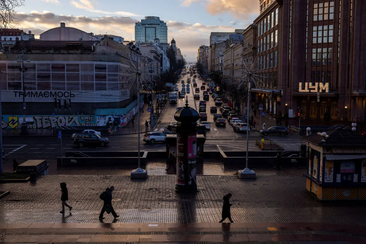 People walk along Khreshchatyk street as the evening sun breaks through the clouds after a rainy day in Kyiv