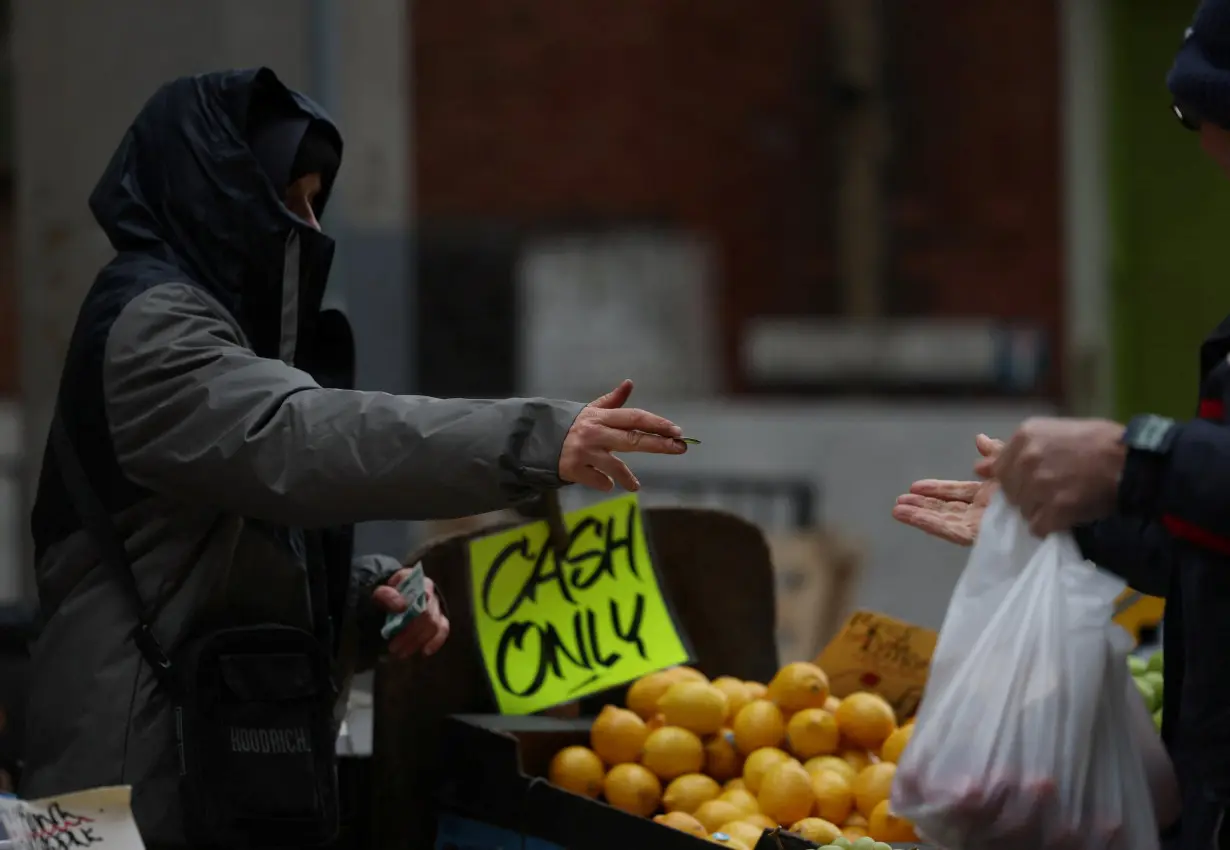 A worker returns cash to a customer after buying produce from a stall on Surrey Street market in Croydon