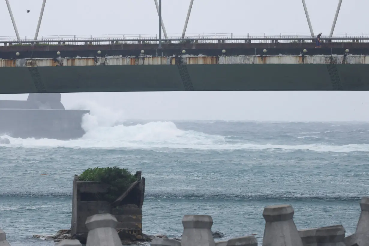 A person walks on a bridge while waves break on the protecting walls nearby as Typhoon Gaemi approaches in Keelung