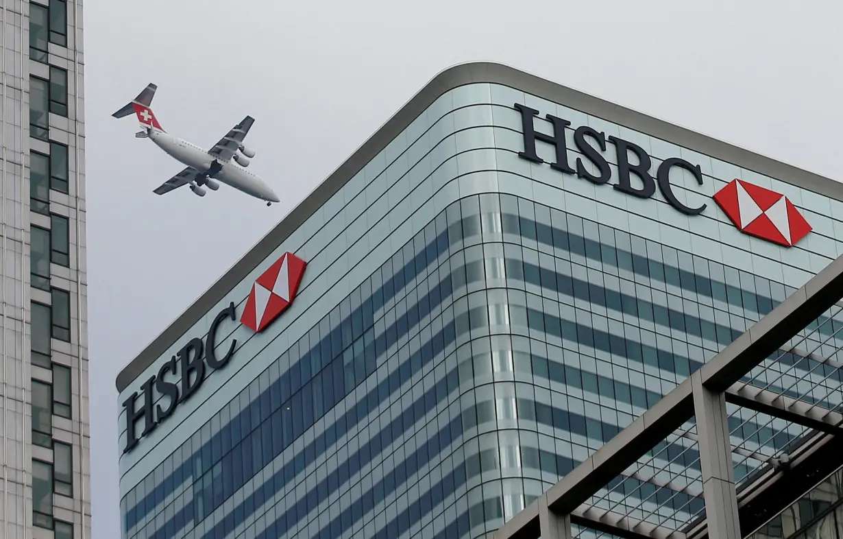 FILE PHOTO: An aircraft flies past the HSBC headquarters building in the Canary Wharf financial district in east London