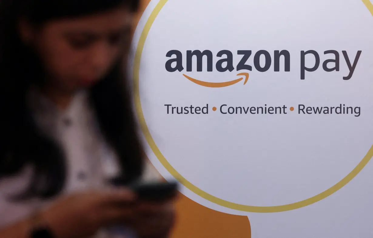 FILE PHOTO: A woman uses her phone next to a logo of the Amazon Pay logo during Global Fintech Fest in Mumbai