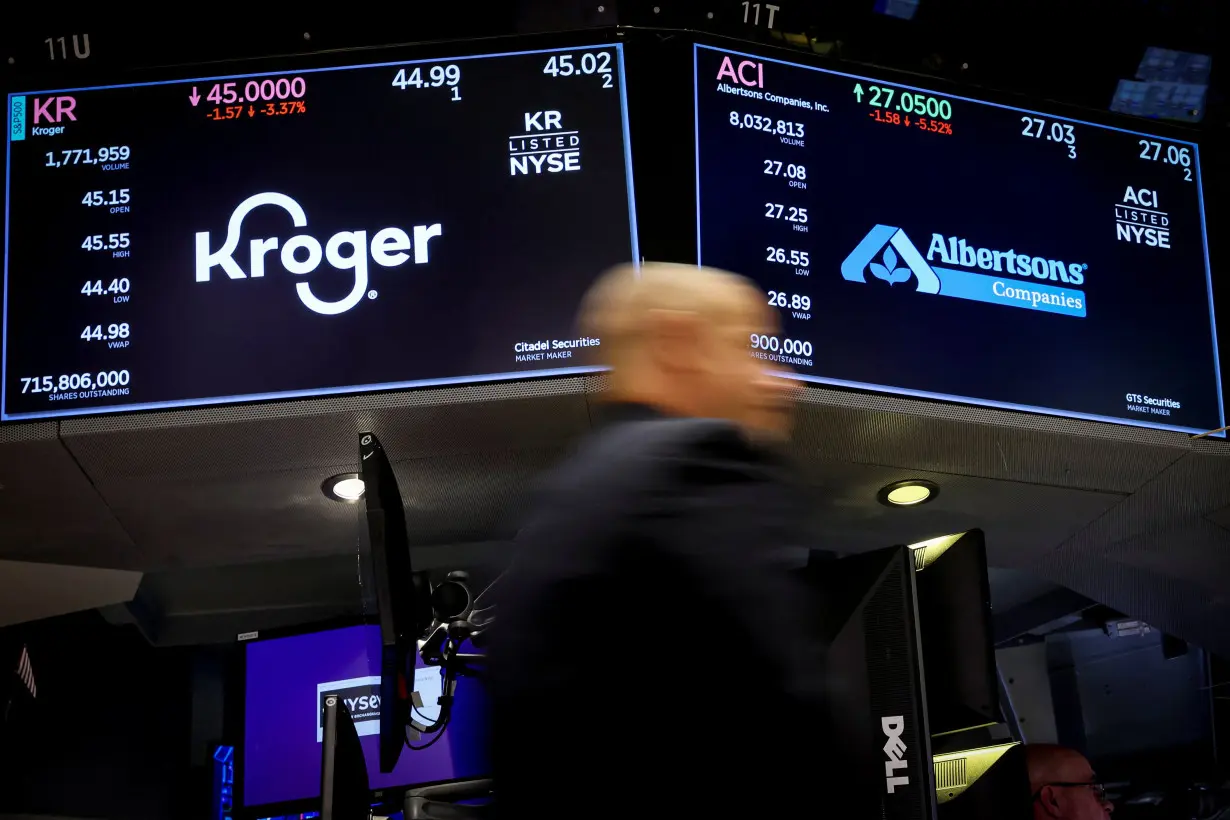 Traders work as screens display the trading information for Kroger and Albertsons on the floor of the NYSE in New York