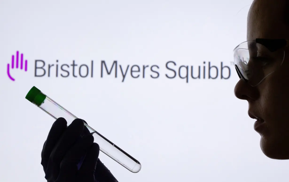 A woman holds test tube in front of displayed Bristol Myers Squibb logo in this illustration