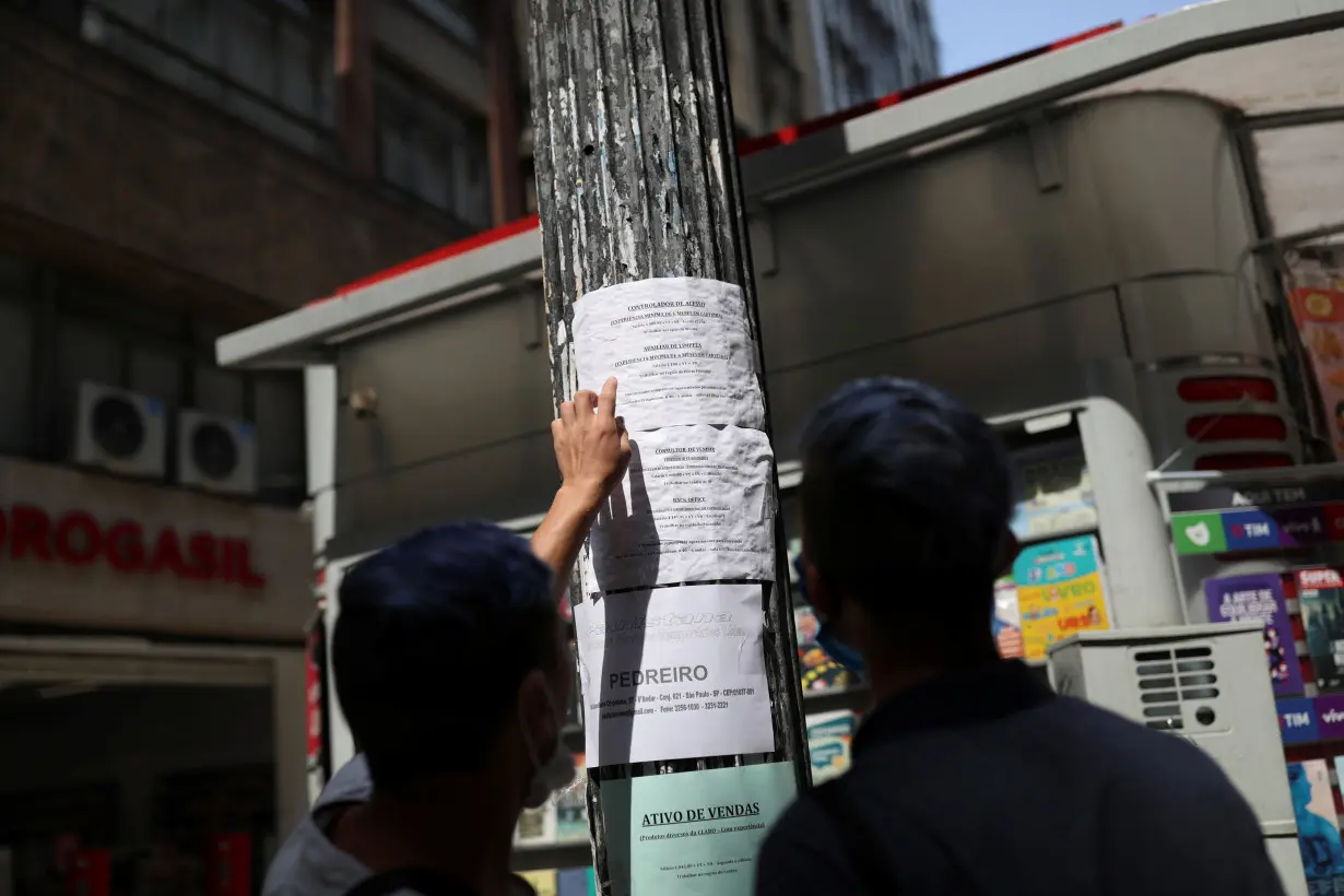 People look at job listings posted on a light pole in downtown Sao Paulo