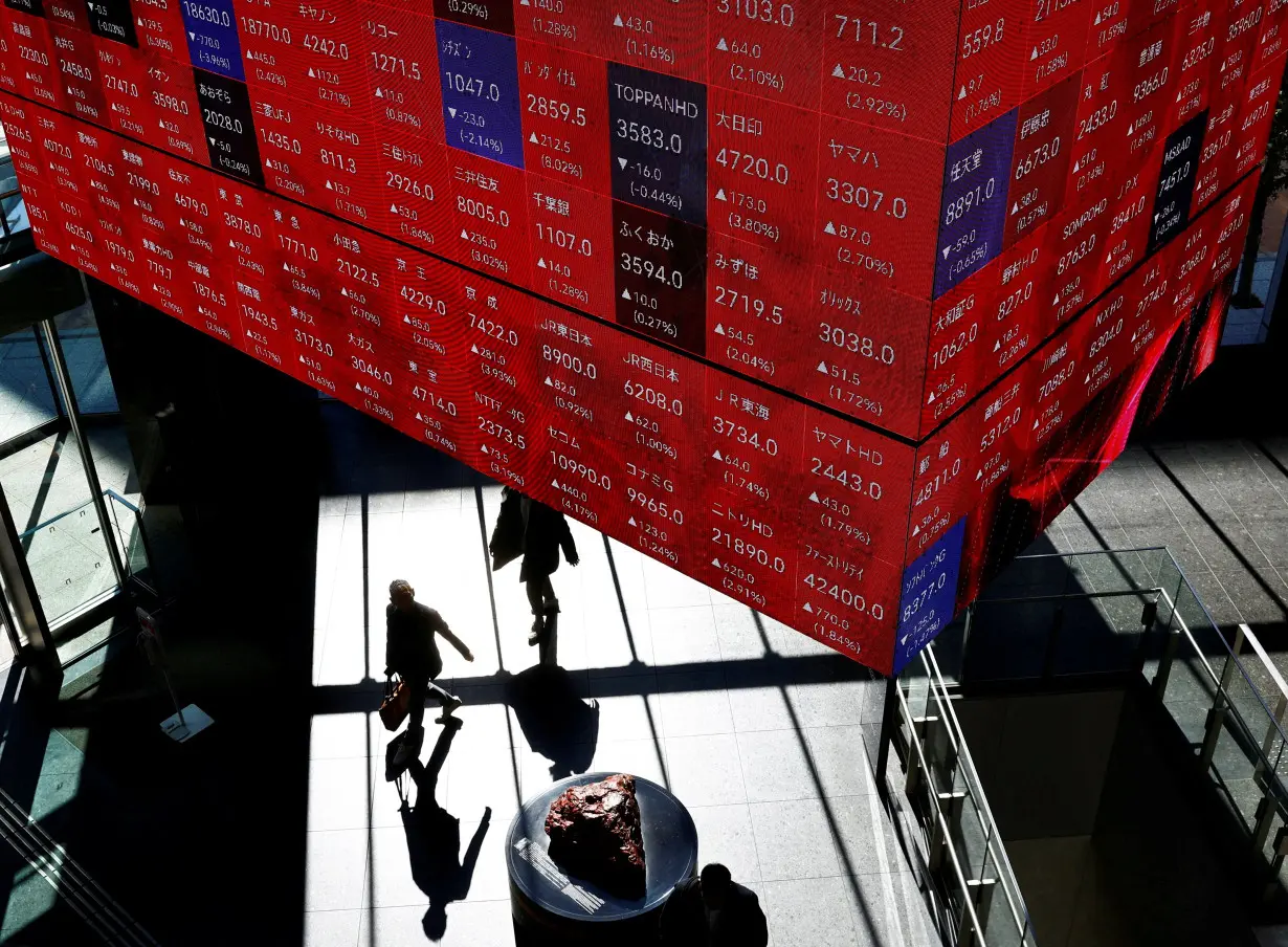 Visitors walk under Japan's Nikkei stock prices quotation board inside a building in Tokyo