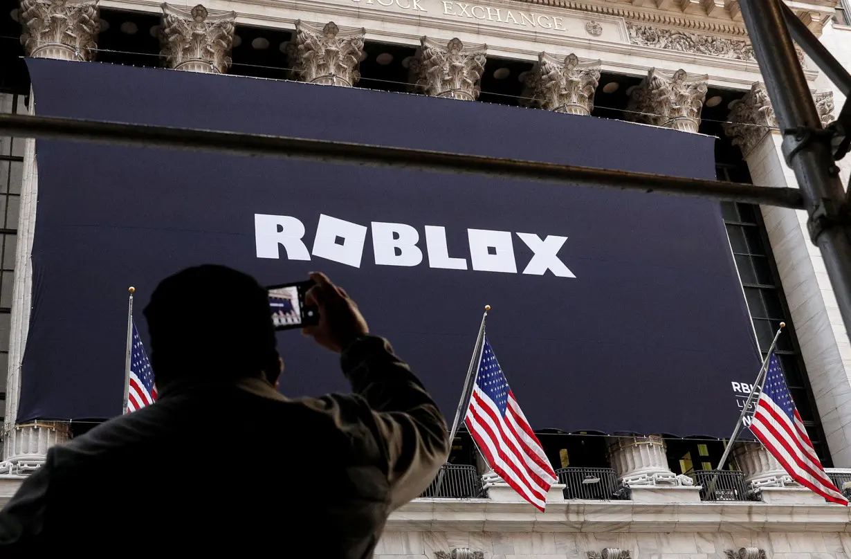 aA man photographs a Roblox banner displayed, to celebrate the company's IPO at the NYSE is seen in New York