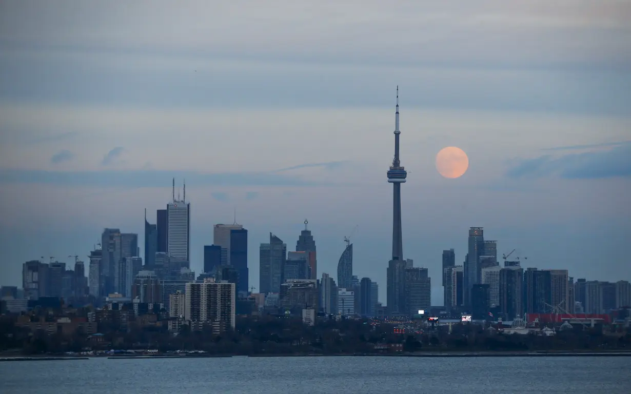 The moon rises behind the CN Tower, a Canadian landmark, and the skyline in Toronto, Canada