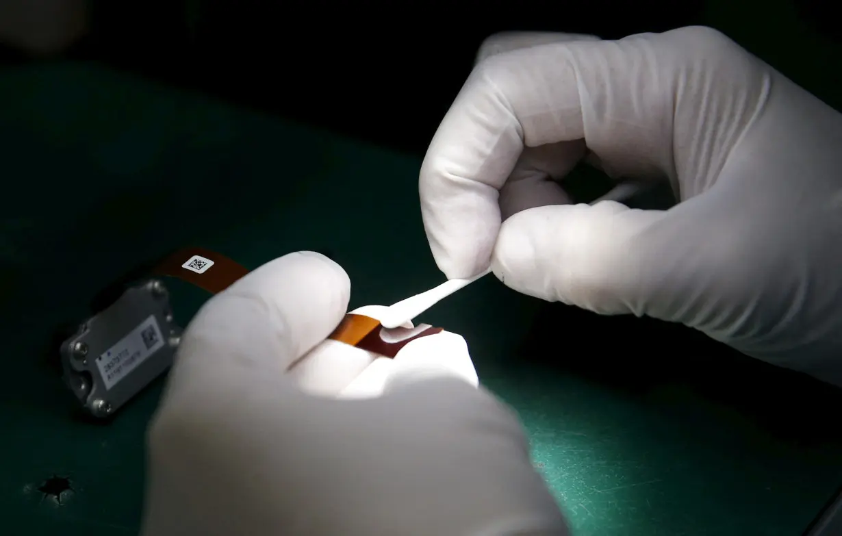 FILE PHOTO: A worker of Ayala Corp's Integrated Micro-Electronics Inc. (IMI) wipes an automotive computer component part at an electronics assembly line in Binan, Laguna