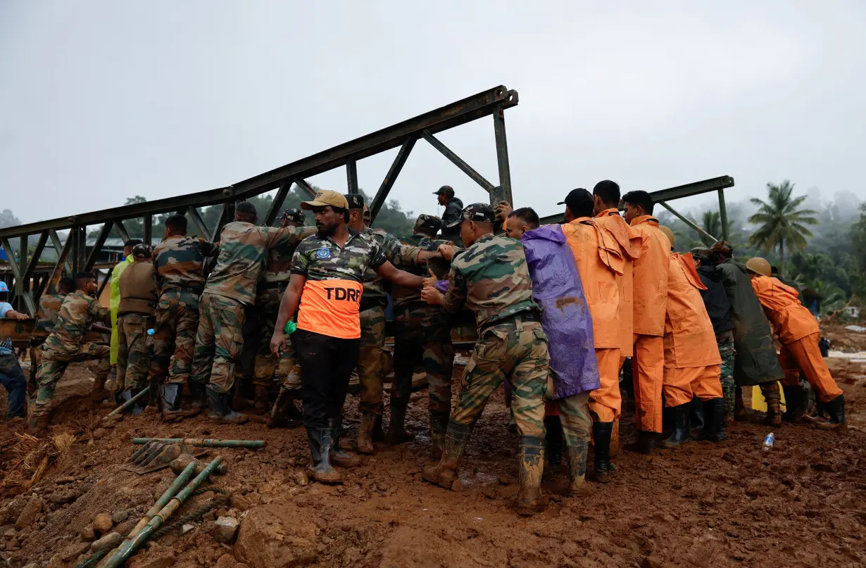 Army personnel and volunteers lift a portion of a bridge during its construction in Wayanad district in the southern state of Kerala