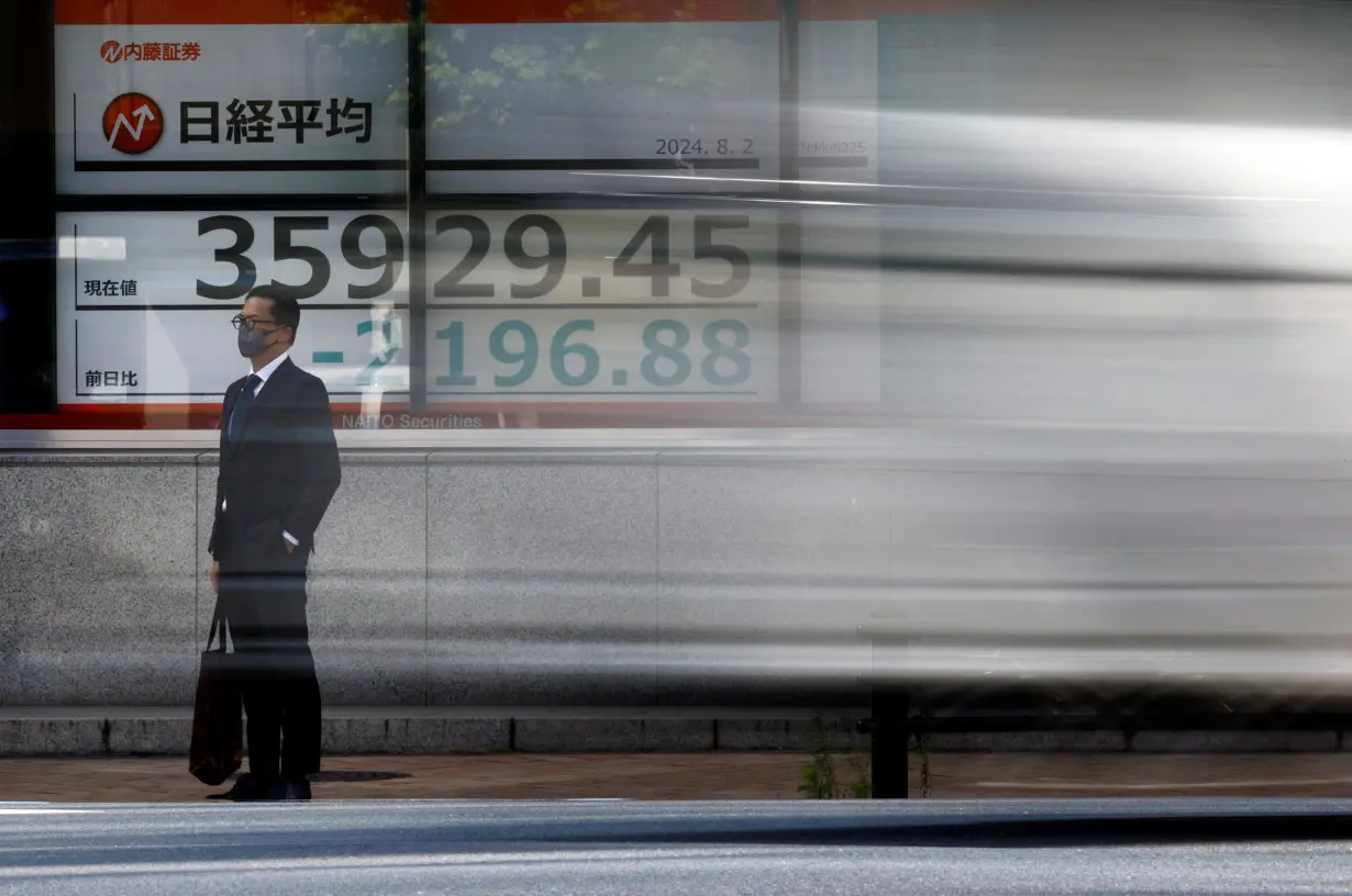 A man stands in front of an electronic screen displaying Japan's Nikkei share average in Tokyo