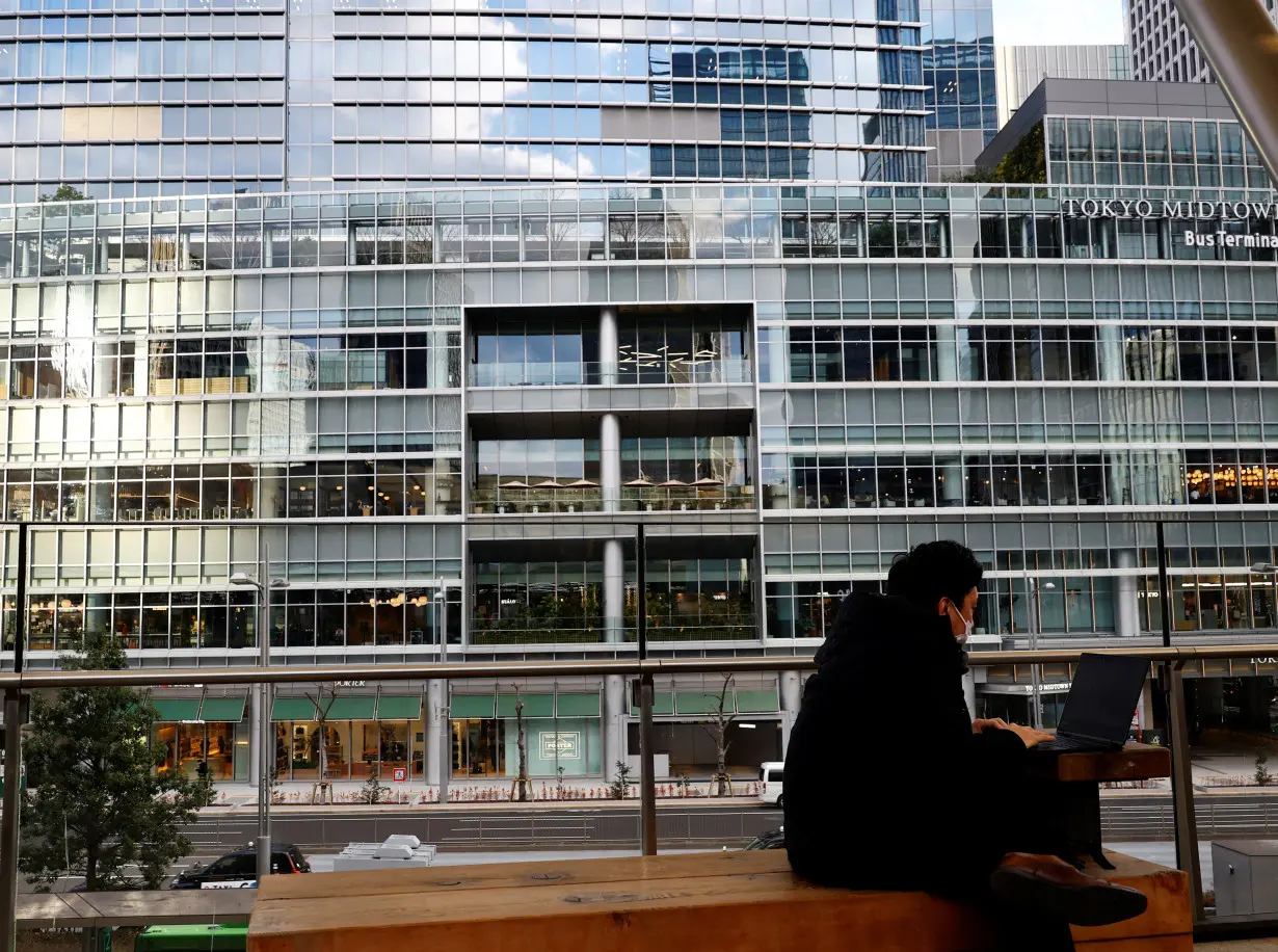 A man uses a laptop on a bench at a business district in Tokyo