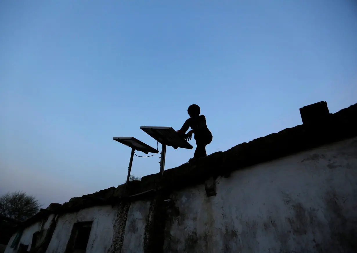 FILE PHOTO: A boy dusts off a solar panel installed on the rooftop of his house on the outskirts of Ahmedabad