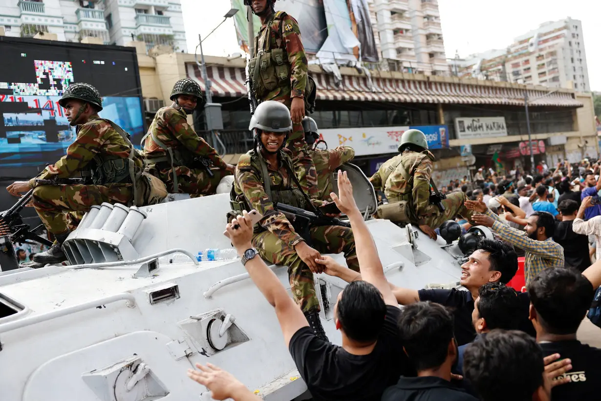 People shake hands with army personnel as they celebrate the resignation of Bangladeshi Prime Minister Hasina in Dhaka