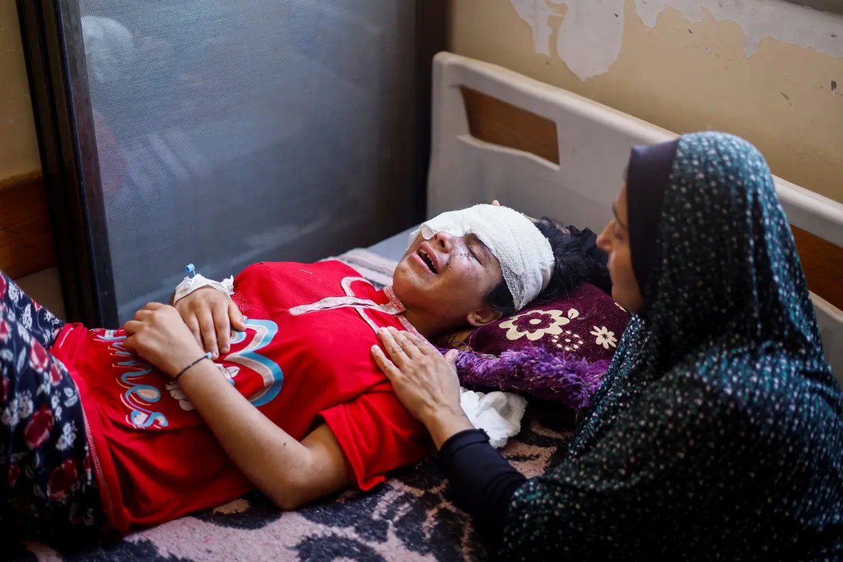 Palestinian girl Maisa Al-Ghandour, who was wounded in an Israeli strike along with her two siblings and mother, is comforted by her mother as she cries on a bed at Nasser hospital, in Khan Younis in the southern Gaza Strip