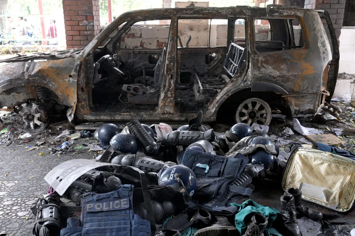 Damaged riot gear of security forces is seen next to a burnt vehicle outside a police station, in Dhaka