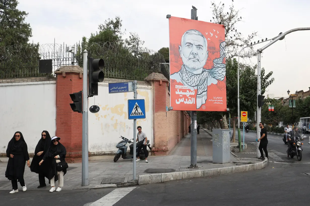 People walk past a banner with a picture of late Hamas leader Ismail Haniyeh in Tehran