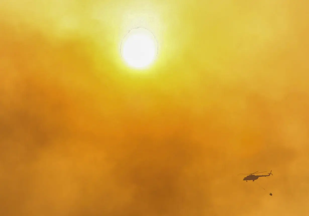 A firefighting helicopter flies through the smoke near Marmaris