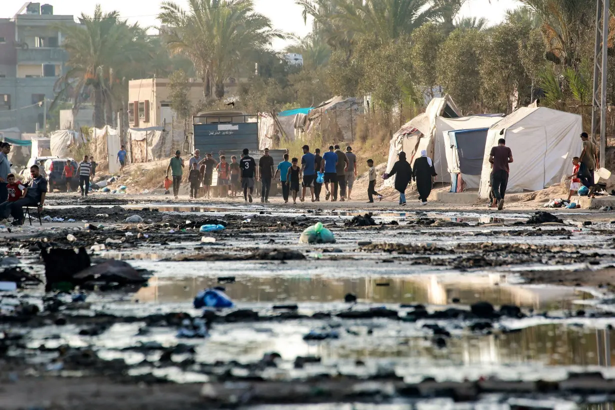 Palestinians walk near tents used as shelter along a street covered with stagnant wastewater in Deir el-Balah, in the central Gaza Strip on July 19.