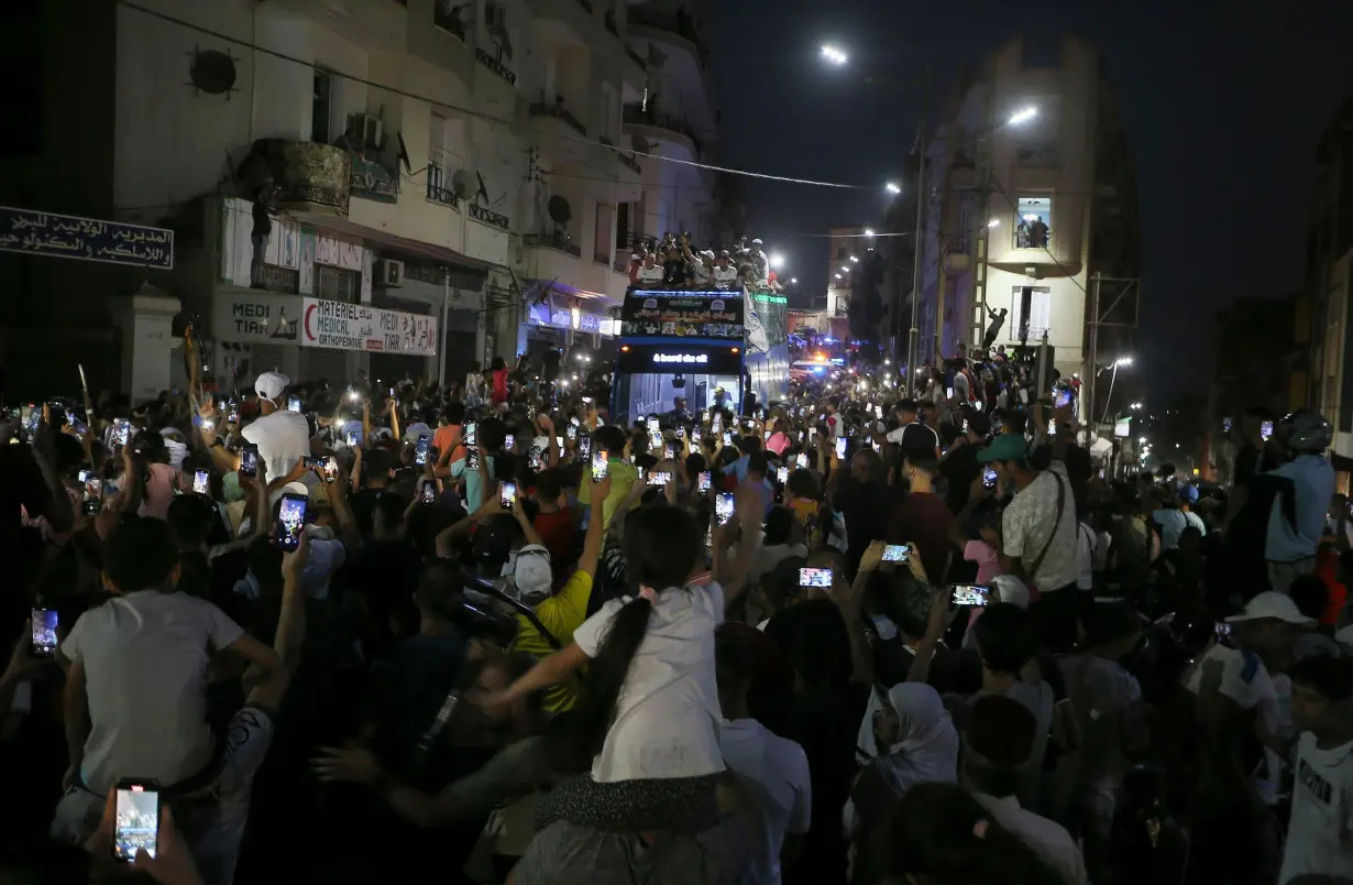 People gather in the streets as Olympic gold medalist Imane Khelif waves from the top of a double decker bus.