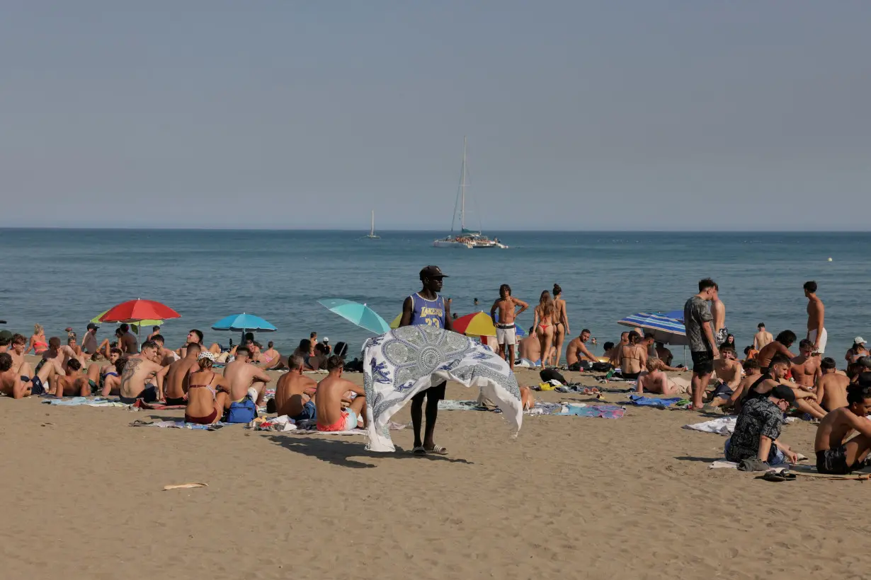 A street vendor holds a cloth as tourists enjoy the weather at Malagueta beach, in Malaga