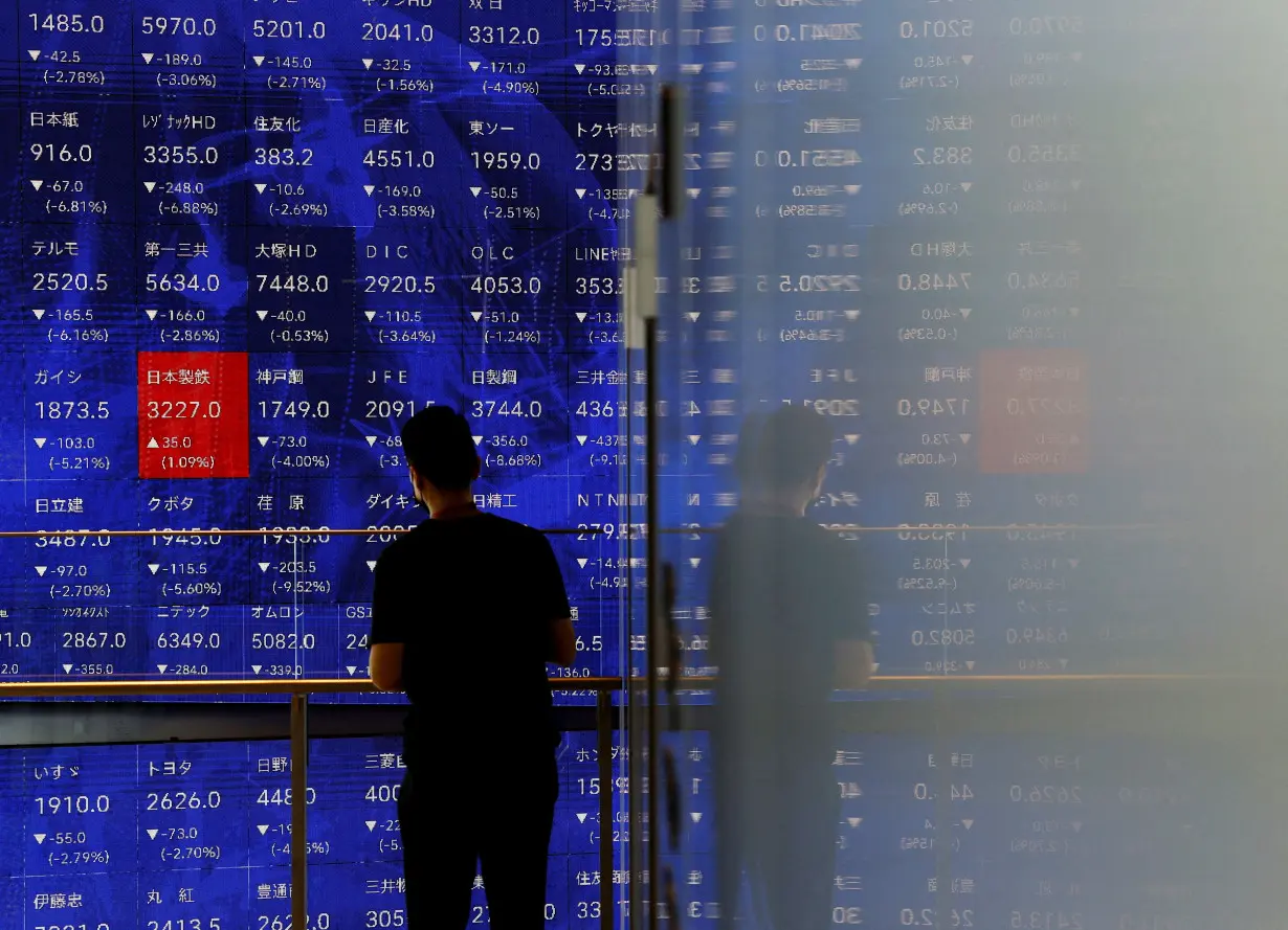 FILE PHOTO: A man stands next to an electronic stock quotation board inside a building in Tokyo, Japan