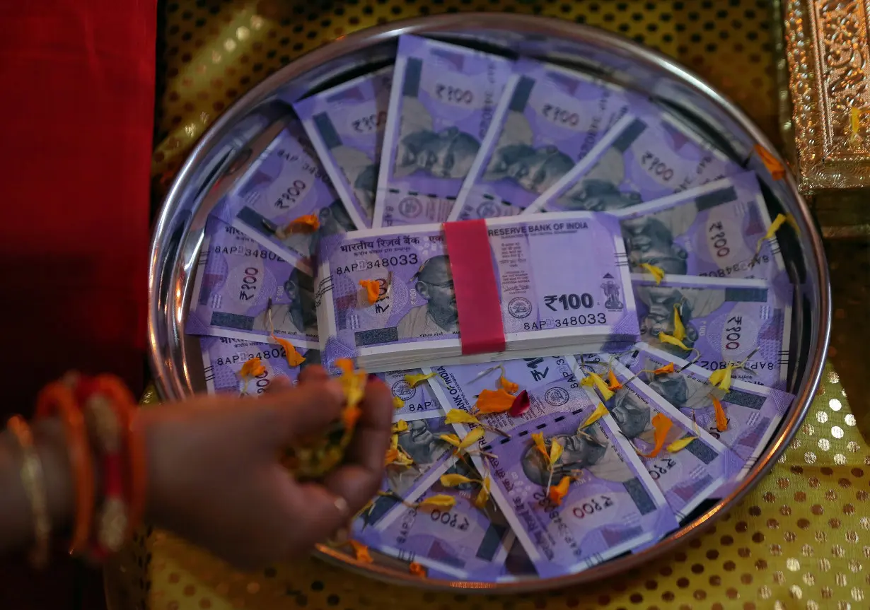 A woman puts flower petals on the new 100 Indian rupee notes as she prays as part of a ritual during Dhanteras, a Hindu festival associated with Lakshmi, the goddess of wealth, in Ahmedabad