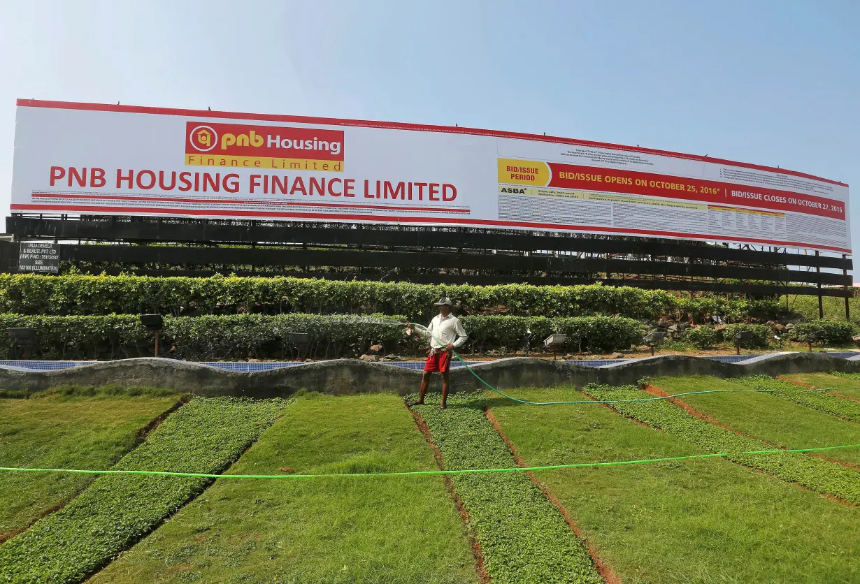 FILE PHOTO: A gardener waters a lawn in front of an advertisement for India's PNB Housing Finance Ltd. initial public offering (IPO) in Mumbai