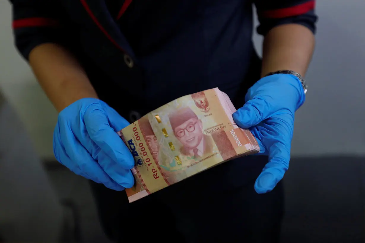 An employee wears synthetic gloves as she counts Indonesia's rupiah banknotes at a currency exchange office in Jakarta