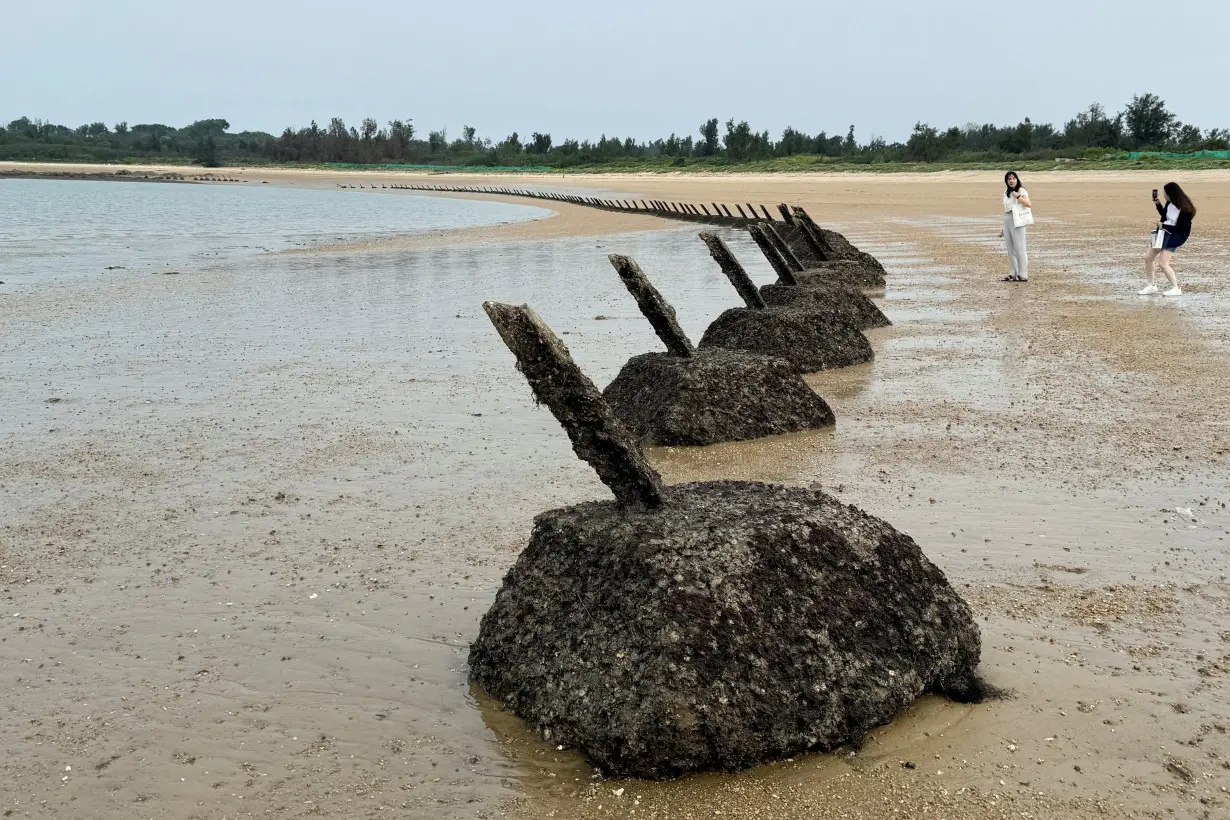 FILE PHOTO: A woman poses for pictures next to anti-landing barricades on a beach in Kinmen Island