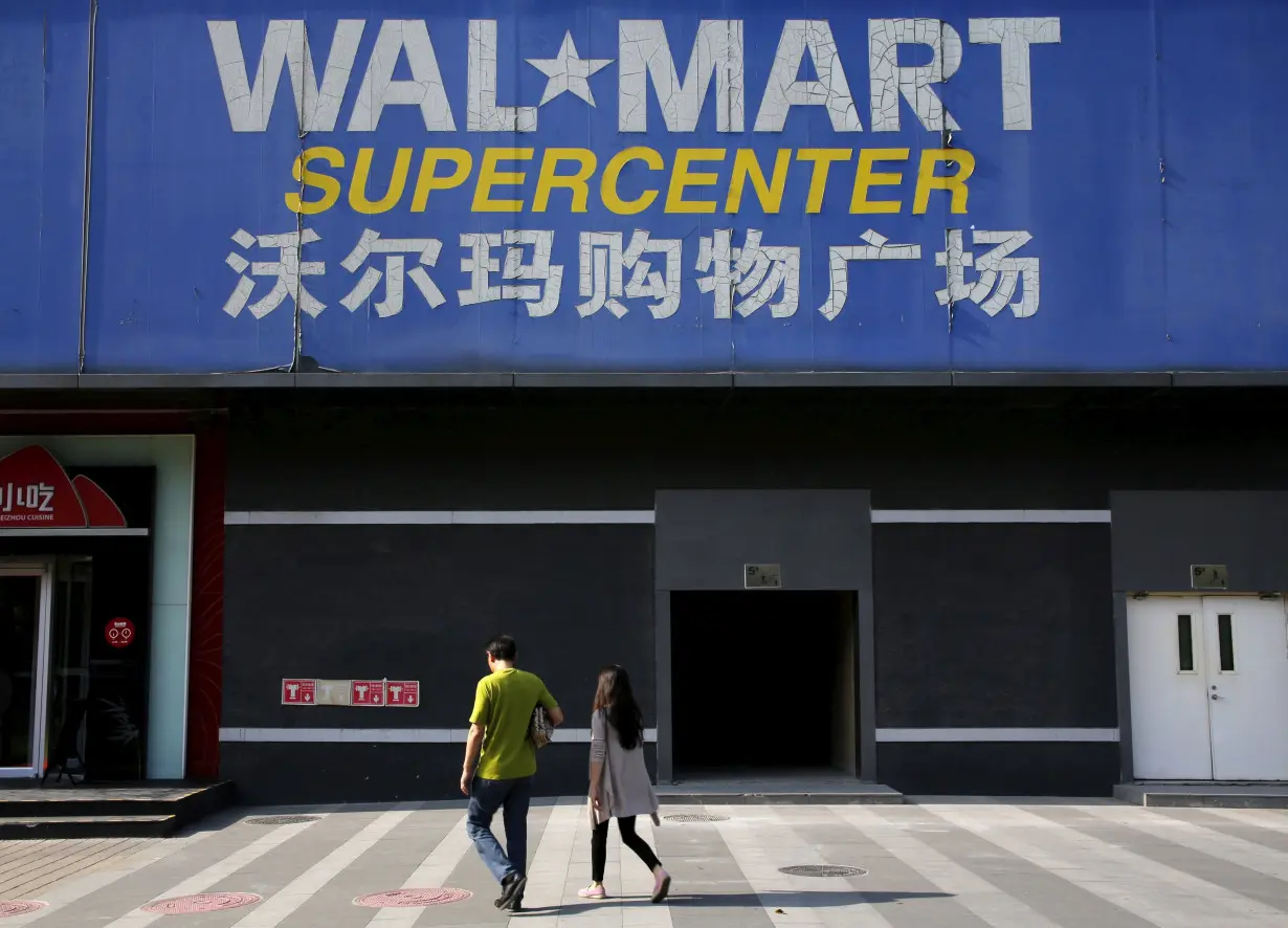 Pedestrians walk past a signboard of Wal-Mart at its branch store in Beijing, China