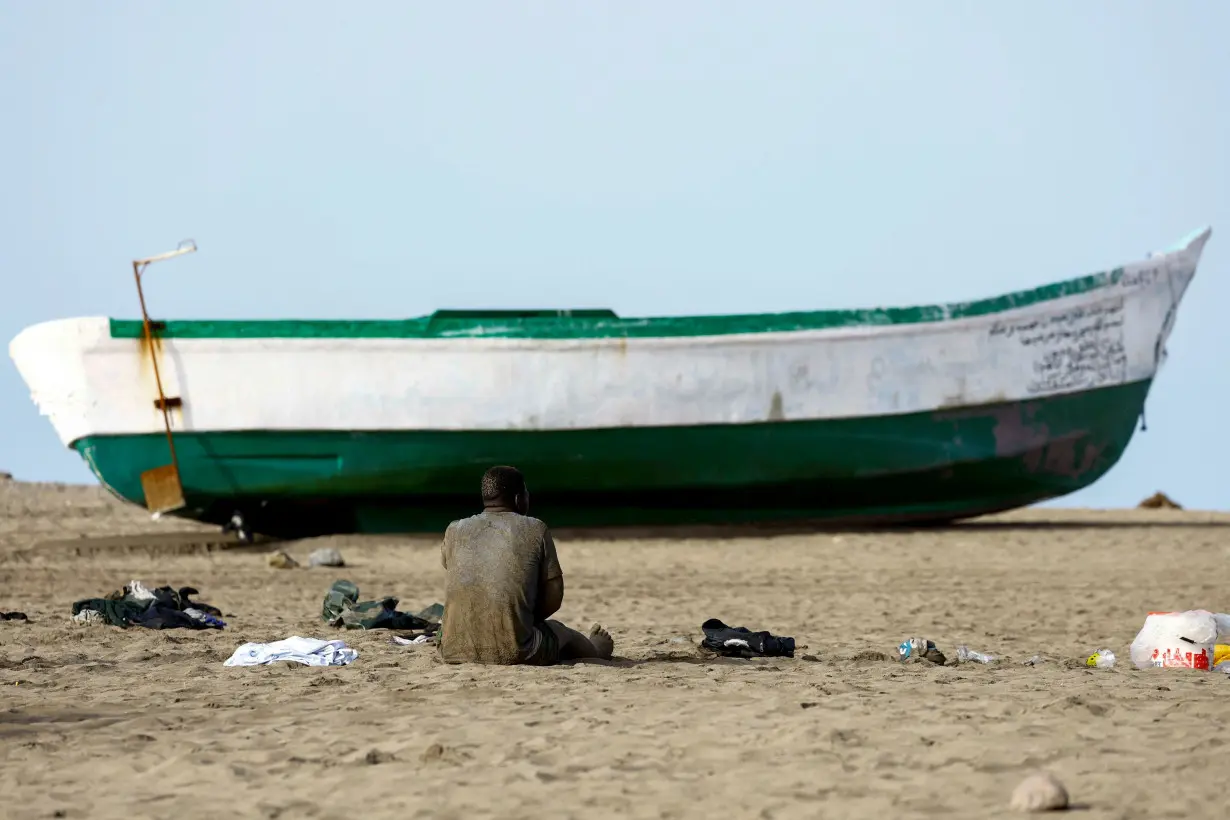 A migrant rests sitting on the sand next to the fiber boat in which he arrived at Las Burras Beach in San Agustin