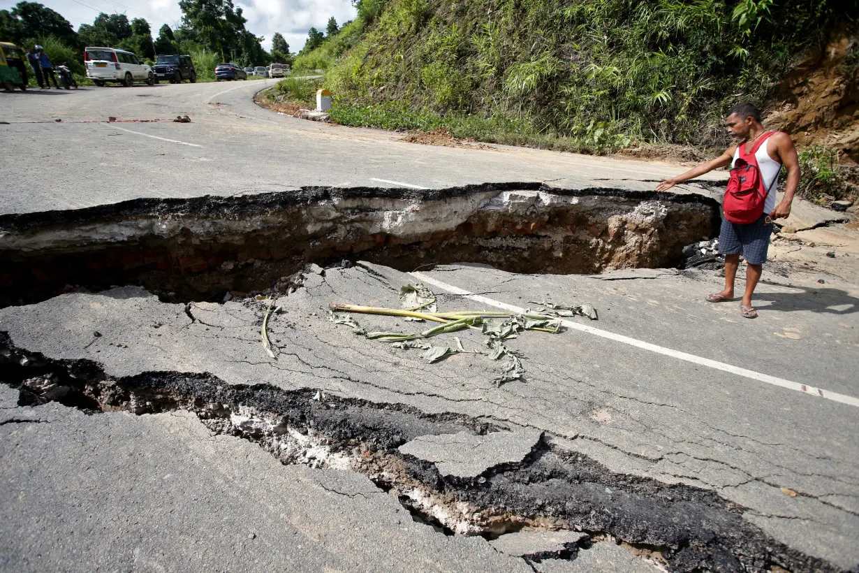 A man gestures next a section of the NH 8 that was damaged by heavy rains in Khowai district