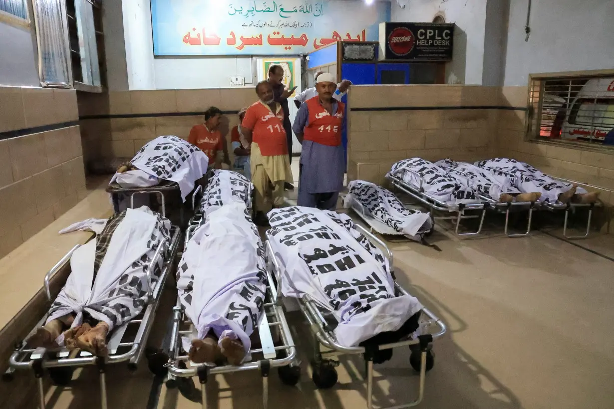 Volunteers stand near the covered bodies of passengers, who were killed after a bus overturned, at the Edhi Foundation morgue in Karachi