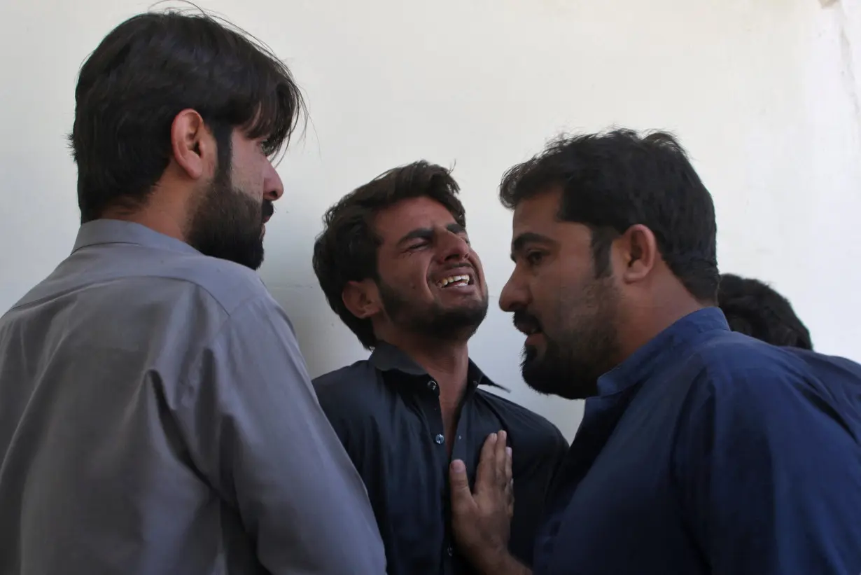 A man is consoled as he waits to receive the body of his father, in Quetta