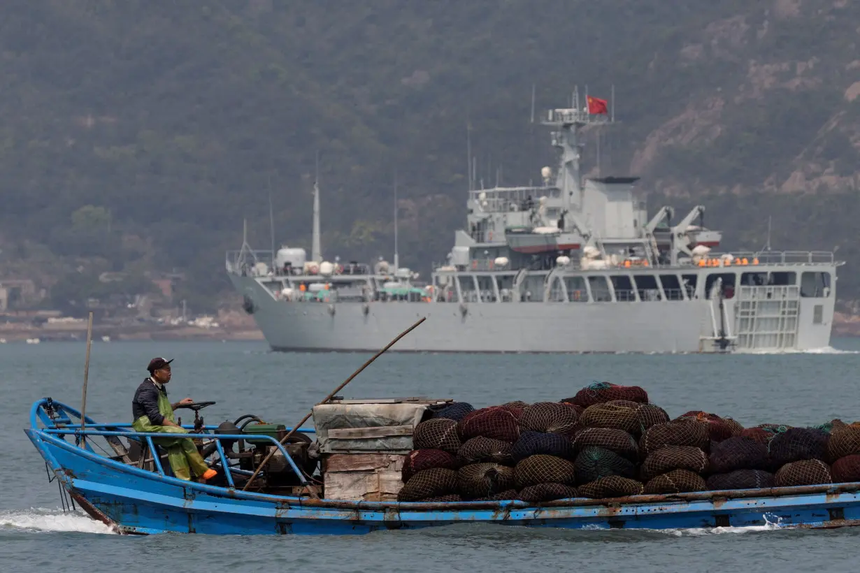 FILE PHOTO: A fishing boat sails past a Chinese warship during a military drill off the Chinese coast near Fuzhou