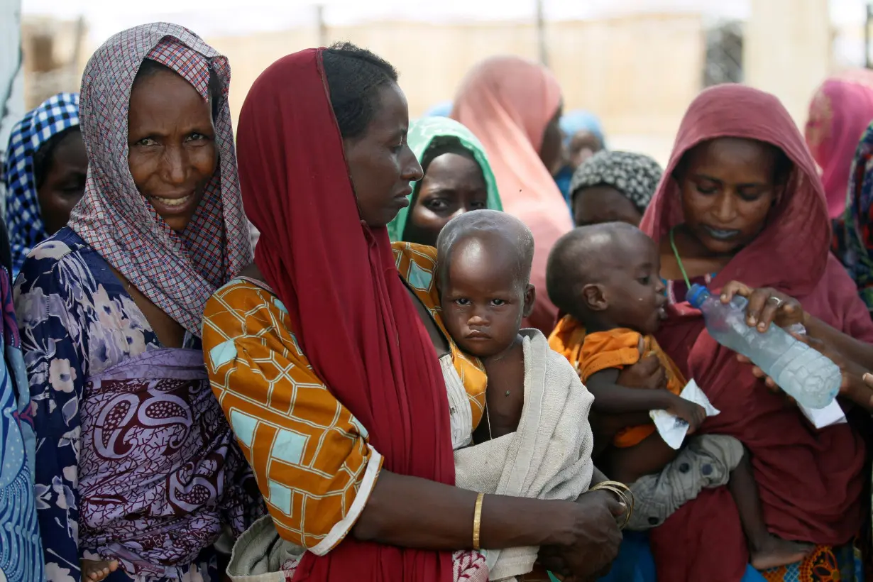 Women wait with their children under a shed for food rations at a internally displaced persons (IDP) camp on the outskirts of Maiduguri, northeast Nigeria