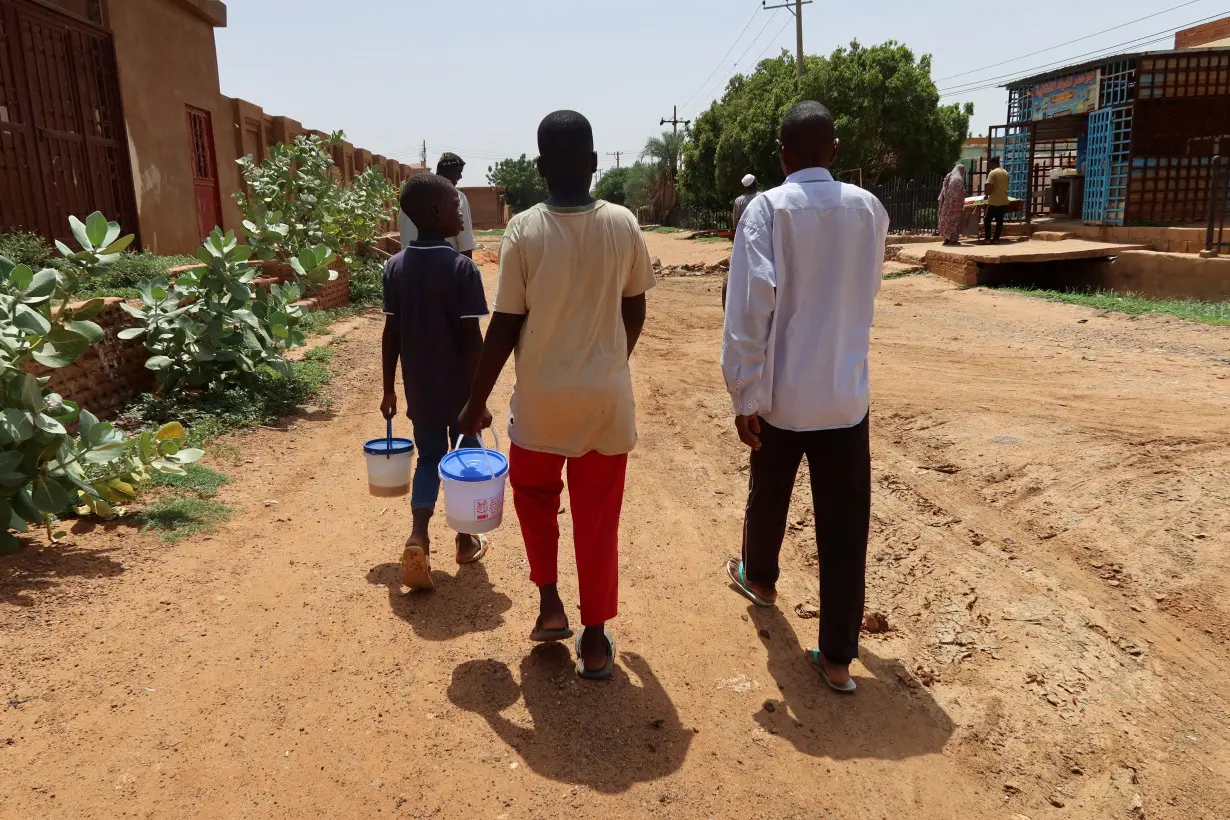 FILE PHOTO: People hold containers filled with food distributed by volunteers in Omdurman