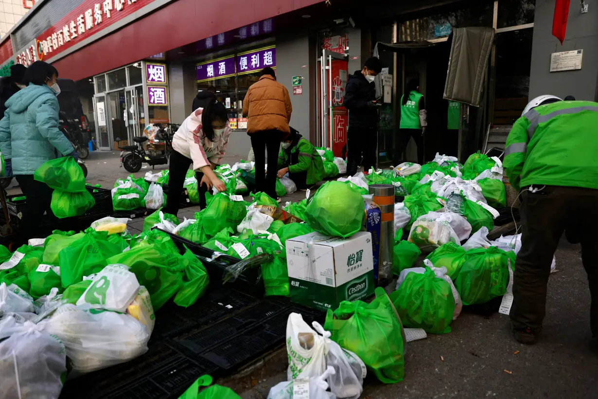 Delivery workers pick up goods of online grocery platform by Meituan in Beijing