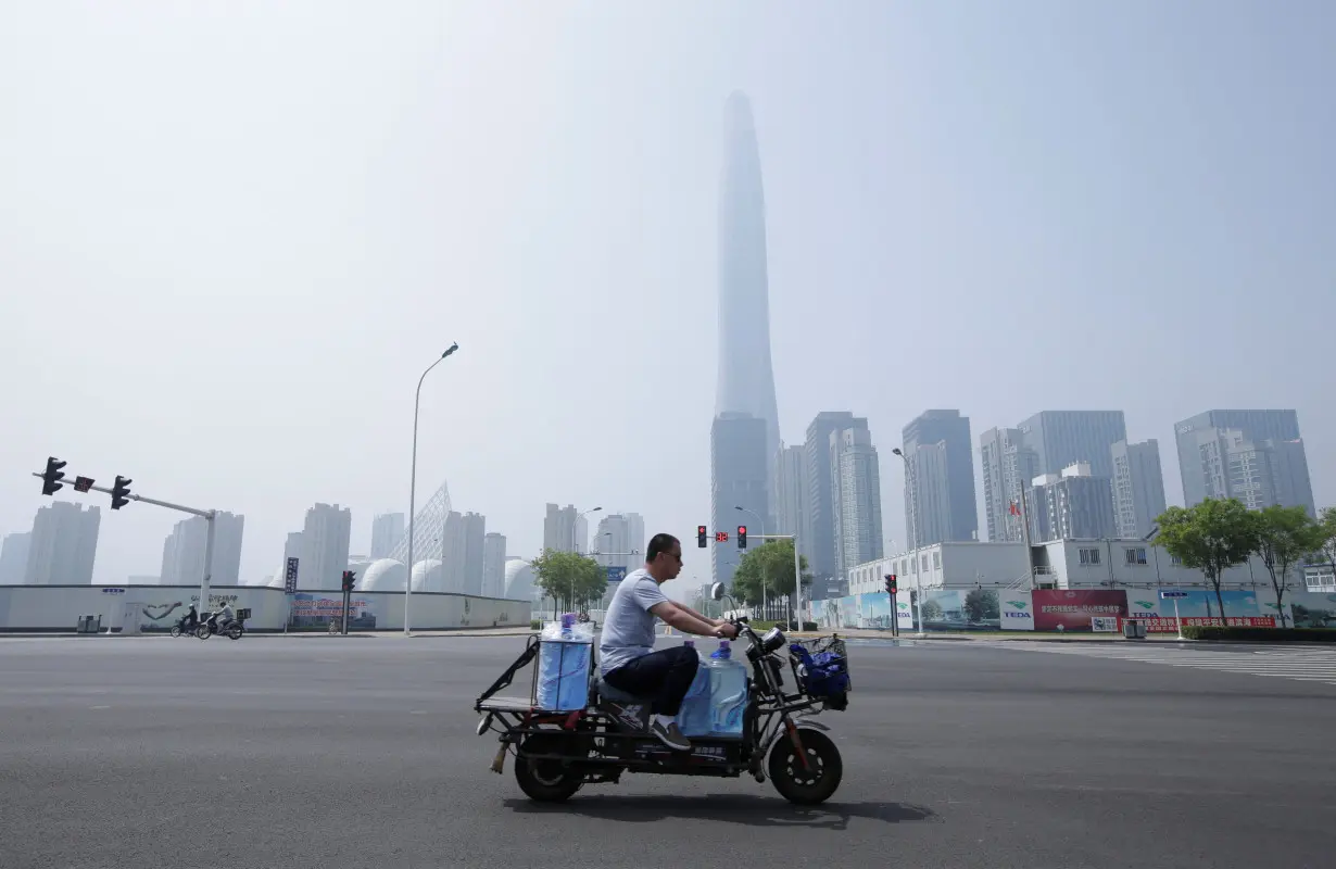 A man rides an electric motorcycle carrying water past Chow Tai Fook Financial Center in Tianjin's Binhai new district