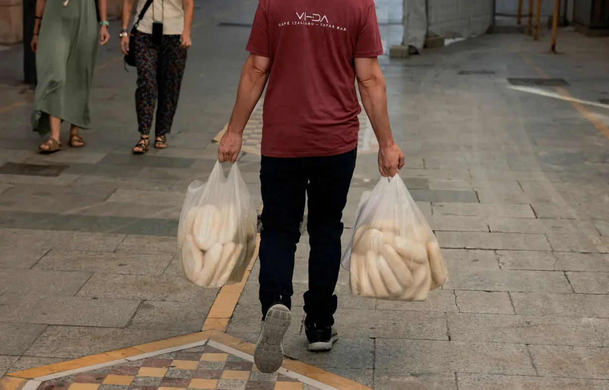 A waiter carries plastic bags with bread along a street in Ronda