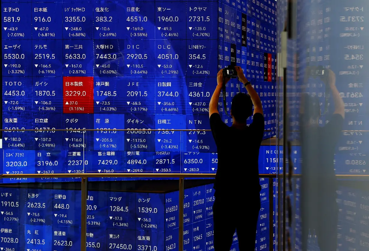 A man takes a photo next to an electronic stock quotation board inside a building in Tokyo