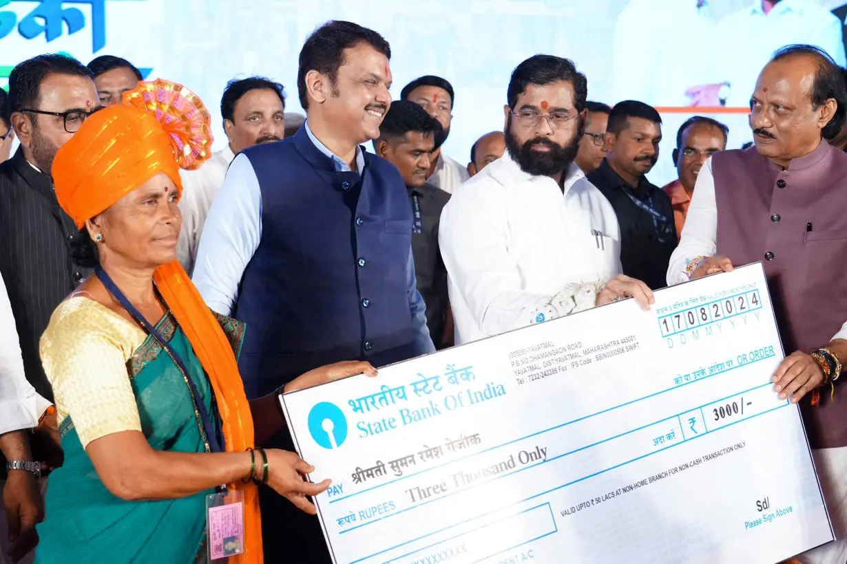 Maharashtra Chief Minister Eknath Shinde accompanied by his deputies Devendra Fadnavis and Ajit Pawar hands a symbolic cheque to a beneficiary of a government welfare scheme, in Kinhi