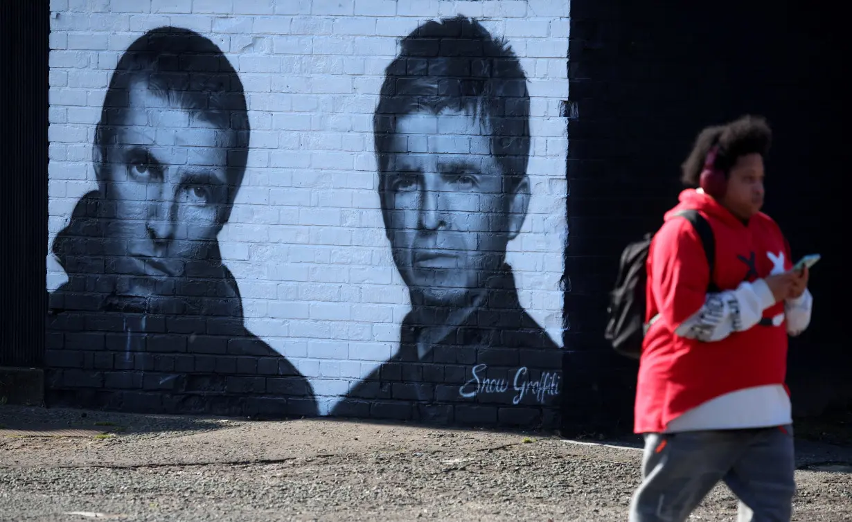 A man walks past a mural of Oasis band members Liam and Noel Gallagher by artist Snow Graffiti on the wall of the Coach and Horses pub in Whitefield, near Manchester