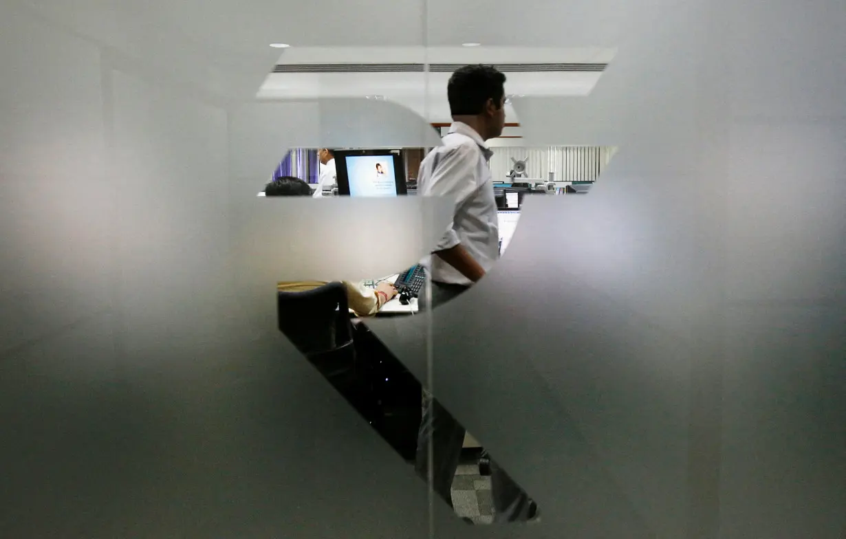 FILE PHOTO: FILE PHOTO: A currency trader is pictured through the symbol for the Indian Rupee on the floor of a trading firm in Mumbai