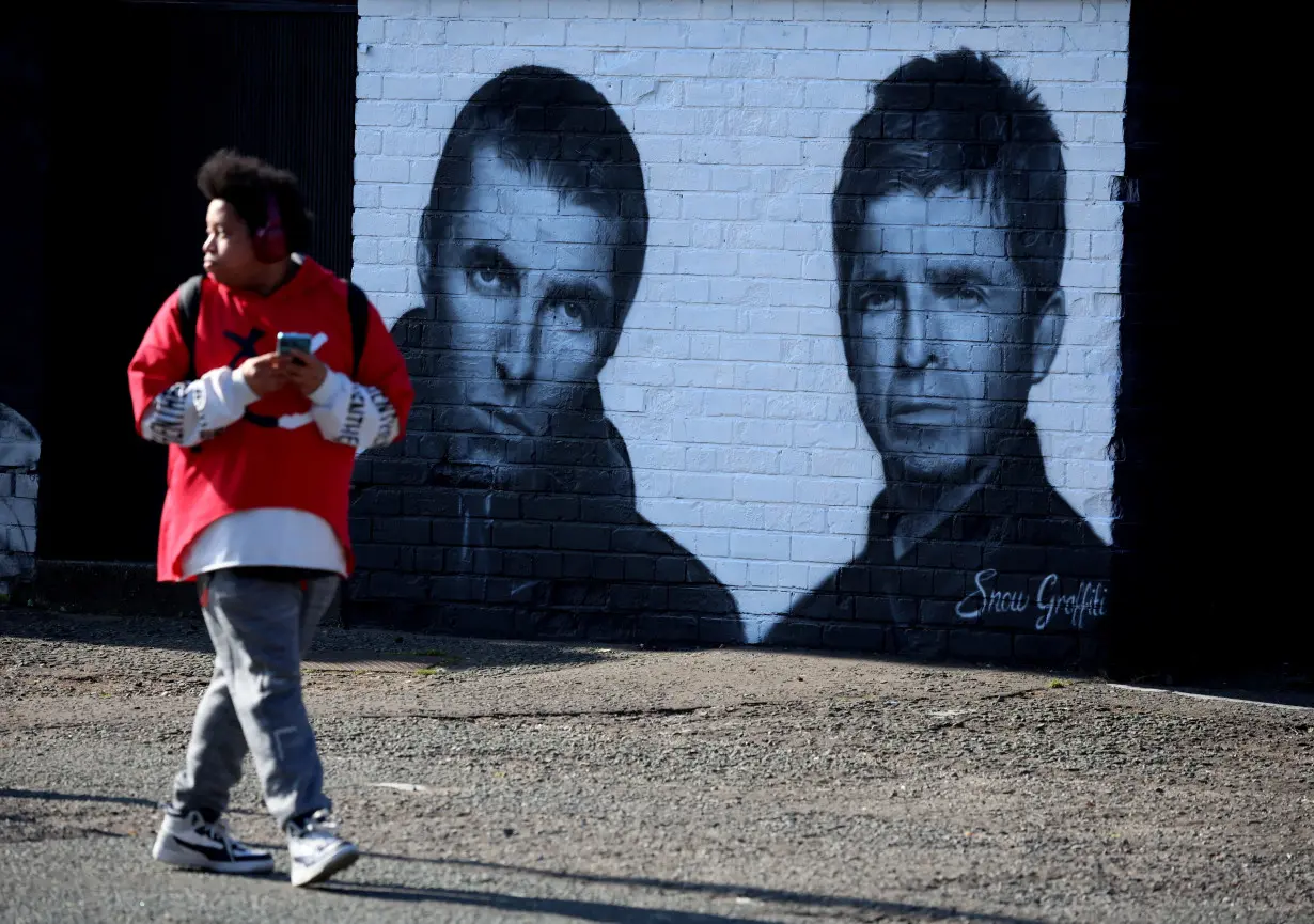 A man walks past a mural of Oasis band members Liam and Noel Gallagher by artist Snow Graffiti on the wall of the Coach and Horses pub in Whitefield, near Manchester