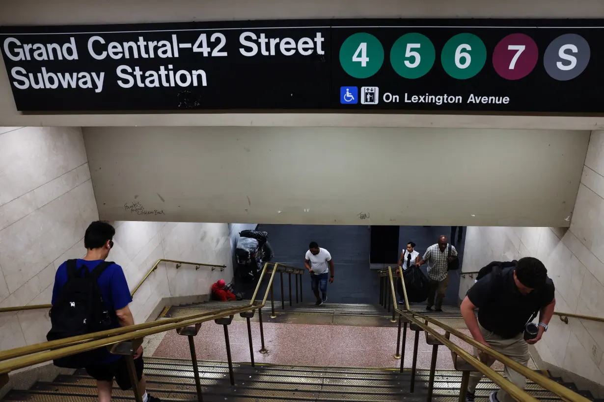 FILE PHOTO: People exit the Grand Central-42 Street subway station as a man sits with his belongings at the bottom of the stairs in New York City