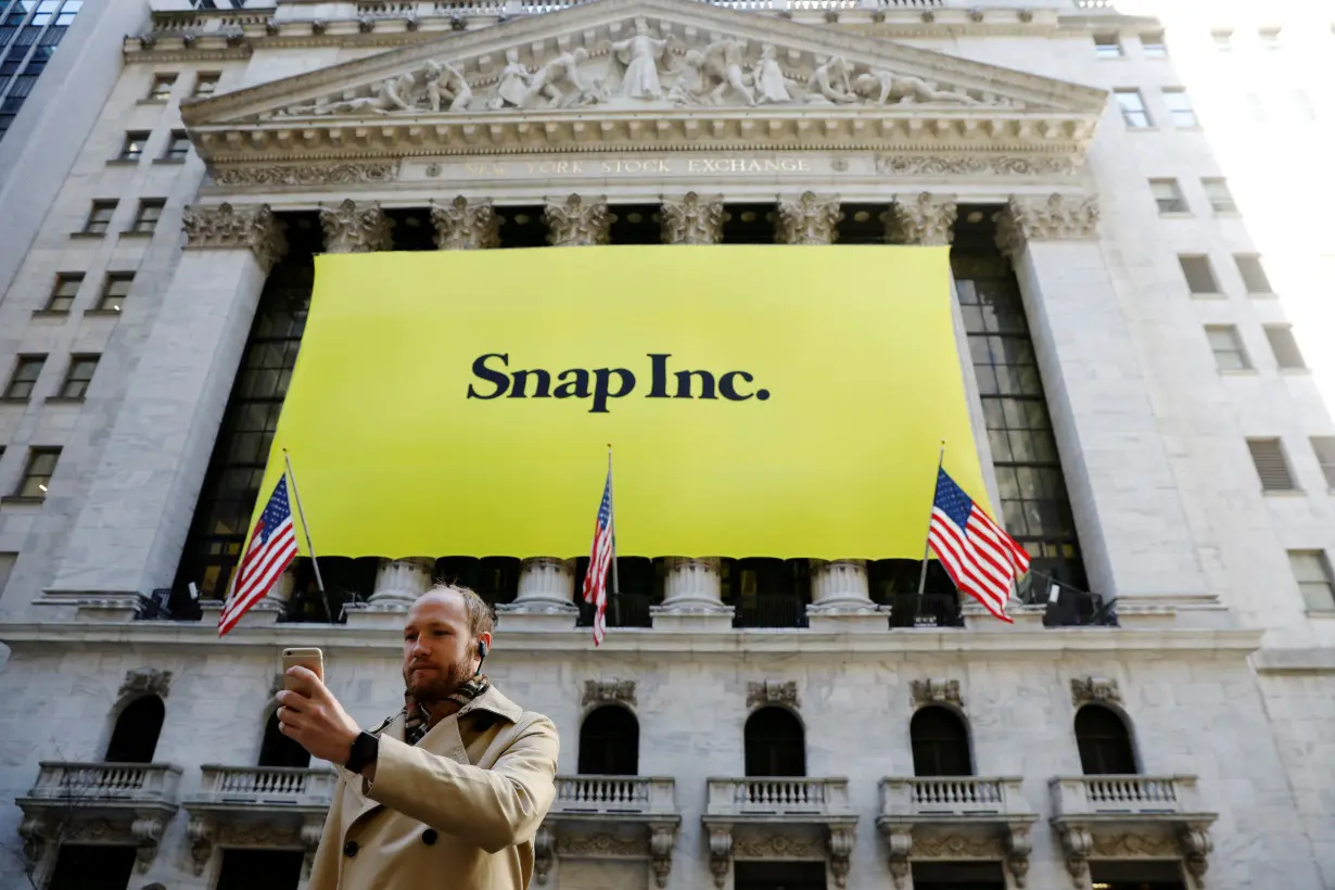 FILE PHOTO: A man takes a photograph of the front of the New York Stock Exchange (NYSE) with a Snap Inc. logo hung on the front of it