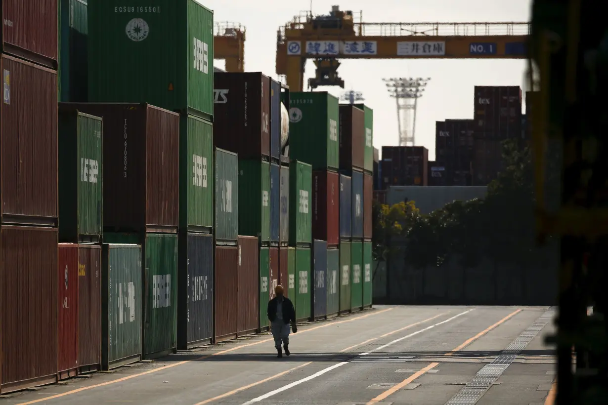 A worker walks between shipping containers at a port in Tokyo